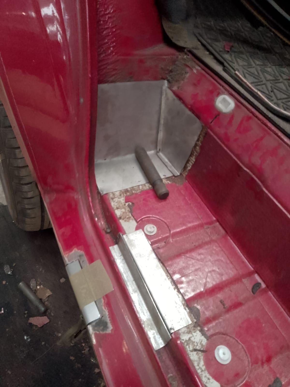 The image captures a close-up of a vehicle's interior door sill with a red-painted metal section, showing visible wear and screws. Recently, MOT welding marks from a mobile welder can be seen on the new metal patch, and a pipe end protrudes from the modified area.
