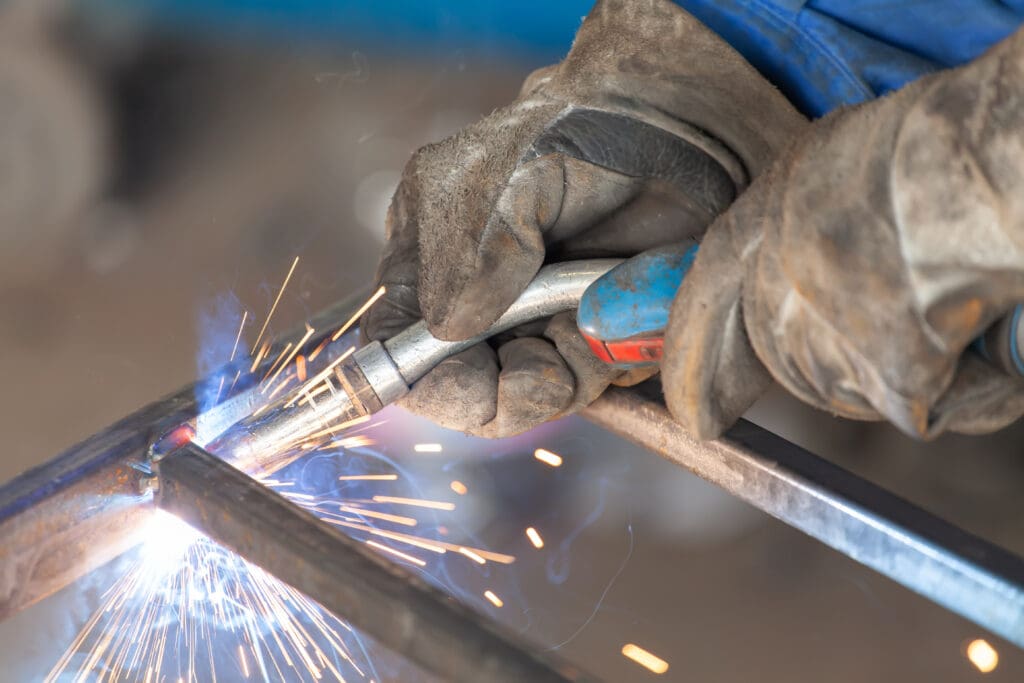 A close-up of a mobile welder skillfully fusing metal pieces, equipped with protective gloves. Bright sparks and blue light from the welding torch create a dynamic scene, highlighting the precision and expertise essential for intricate plant repair tasks.