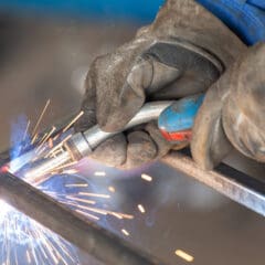 A close-up of a mobile welder skillfully fusing metal pieces, equipped with protective gloves. Bright sparks and blue light from the welding torch create a dynamic scene, highlighting the precision and expertise essential for intricate plant repair tasks.